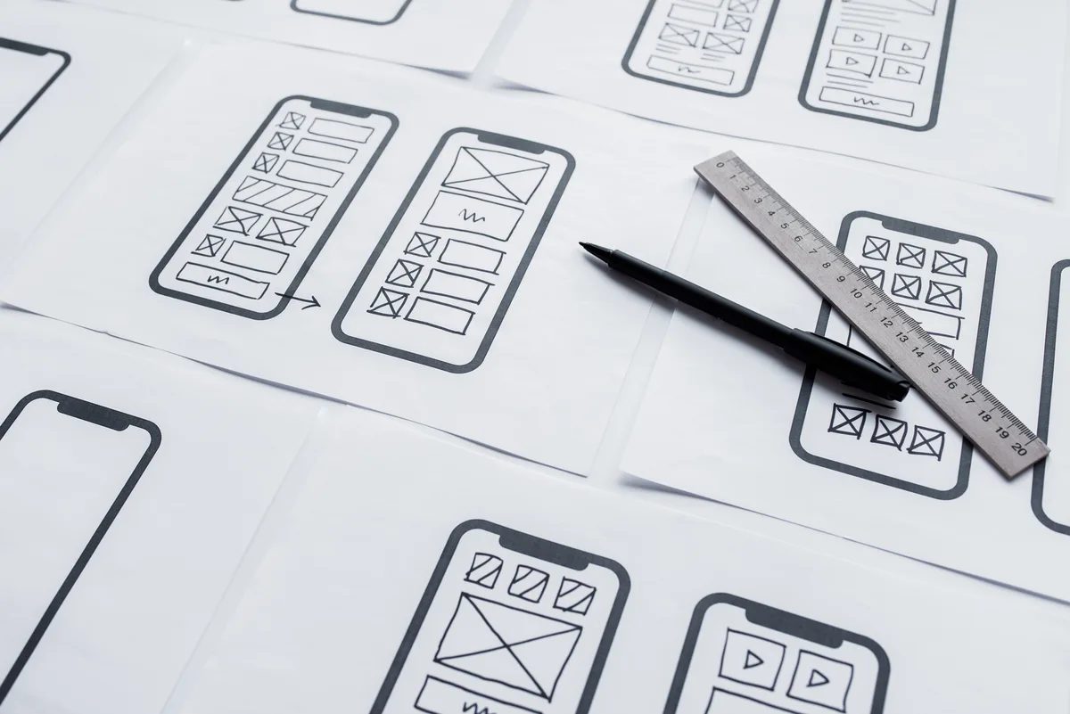 Paper mobile app wireframes with a pen and ruler for planning the user experience.